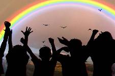 Silhouette of children cheering infron of a rainbow sunset.